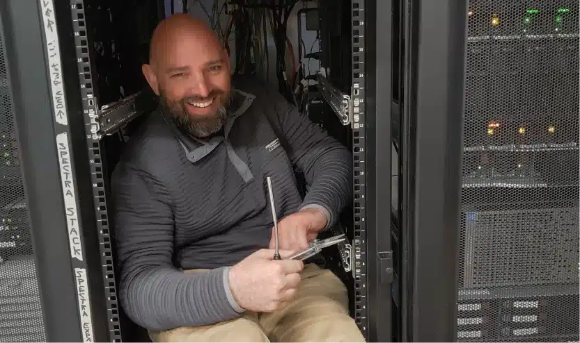 IT professional seated inside network equipment racks handling server repairs with tools in hand