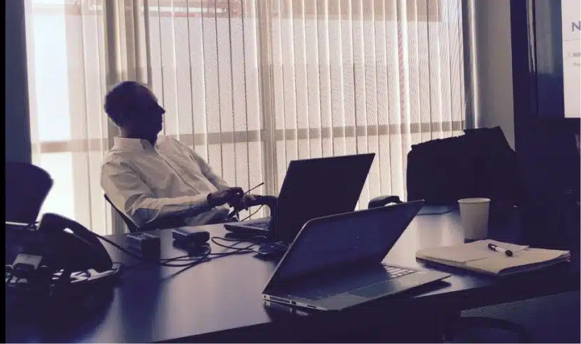 Man seated at a conference table with laptop computers during a business meeting