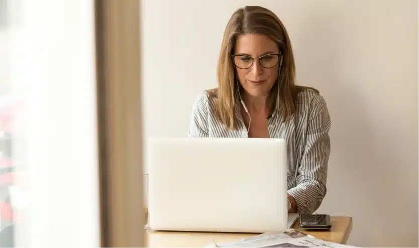 Professional woman wearing glasses working remotely on a white laptop at a home office desk