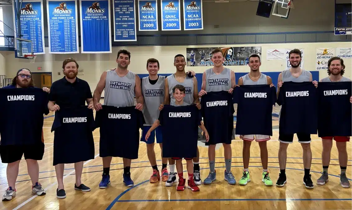 DataPivot Technologies basketball team celebrating victory holding championship shirts inside a gymnasium