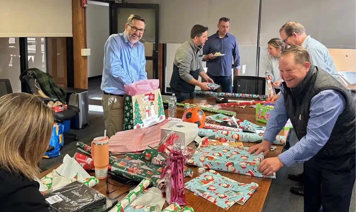 Office team gathered around a table wrapping gifts for a company charity event during Giving Day