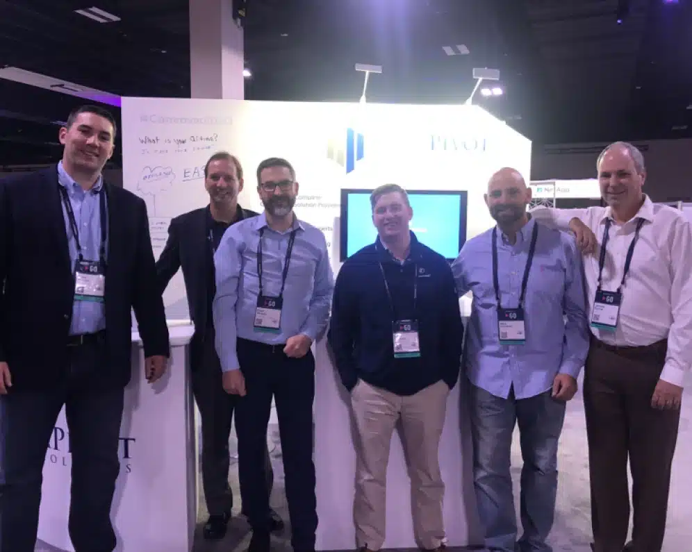 Team of DataPivot Technologies members posing at a technology conference booth with branded signage
