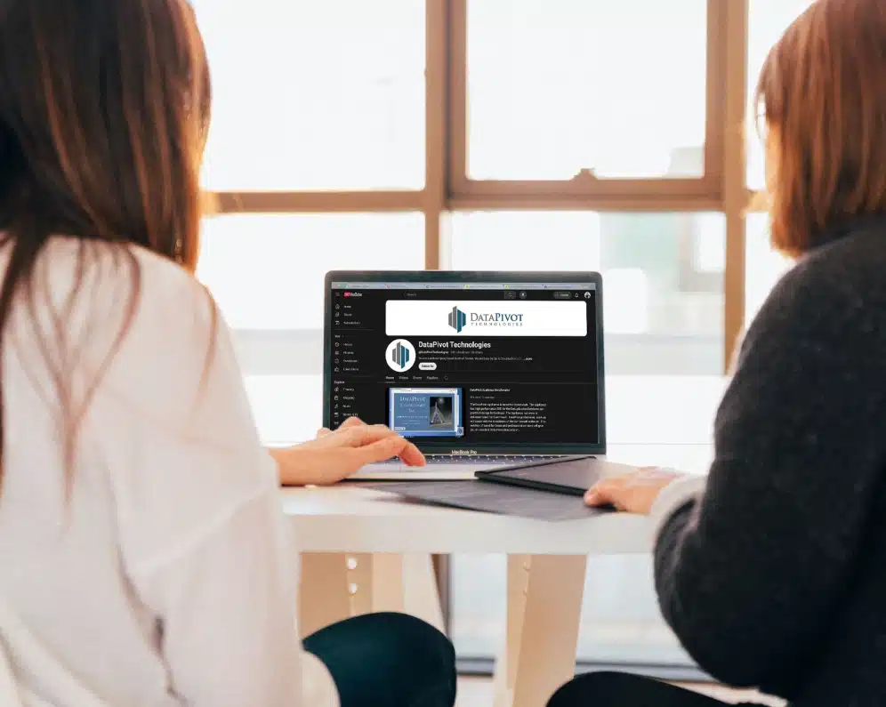 Two women viewing DataPivot Technologies YouTube channel together on laptop in bright office setting