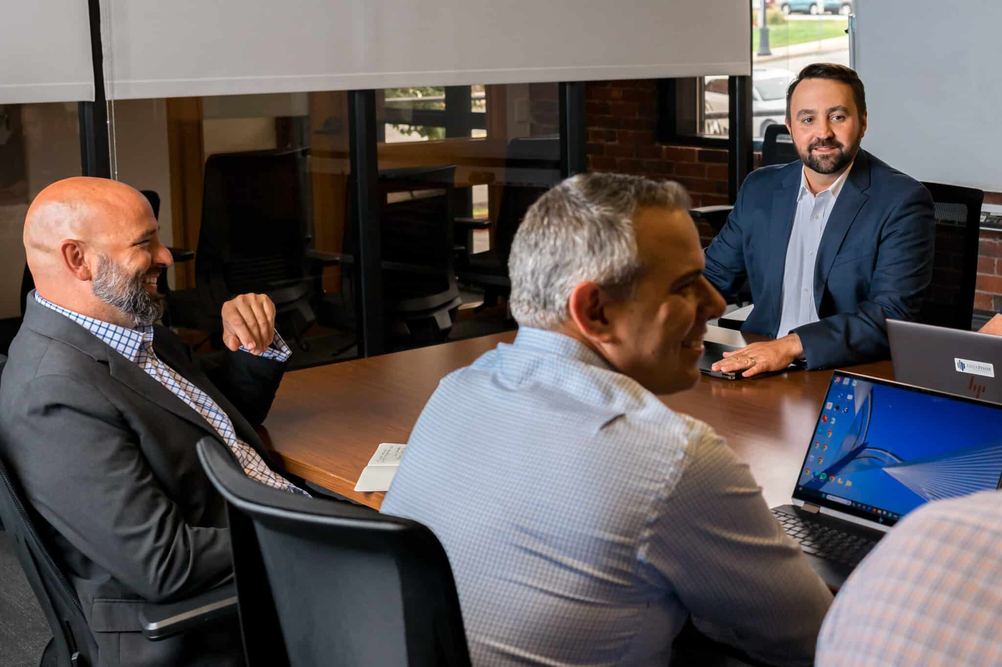Group of business professionals meeting in a conference room with laptops and smiling conversations.