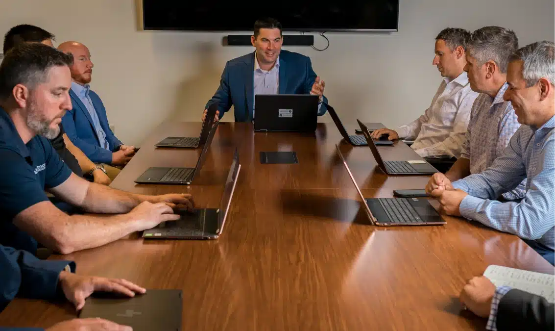 Leadership team engaged in a formal conference room meeting with laptops and collaborative discussion