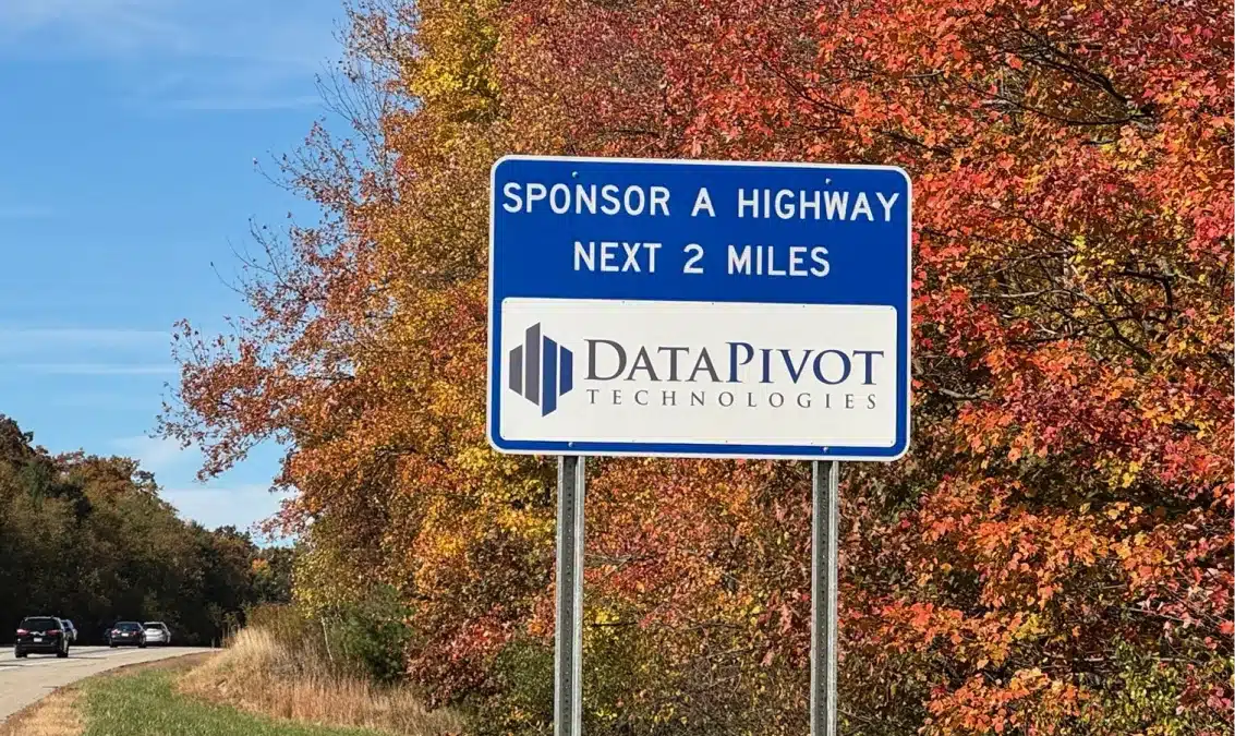 Roadside sponsorship sign featuring DataPivot Technologies logo along a highway with autumn foliage