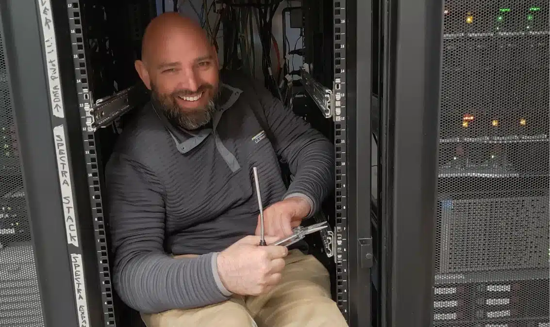 Smiling IT technician working inside server racks during hardware installation and maintenance tasks