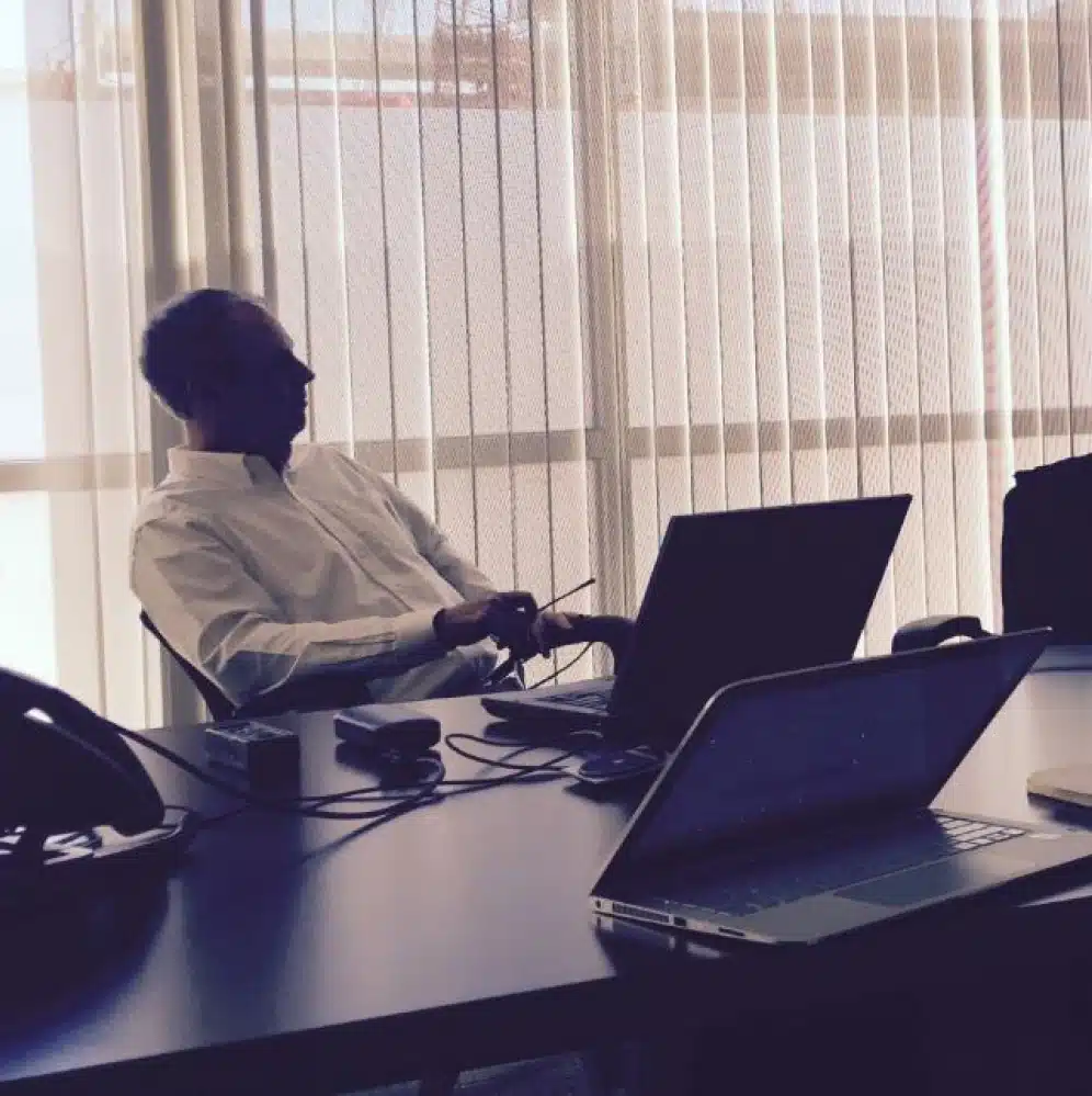 Business professional seated at conference table with visible laptops and devices during meeting